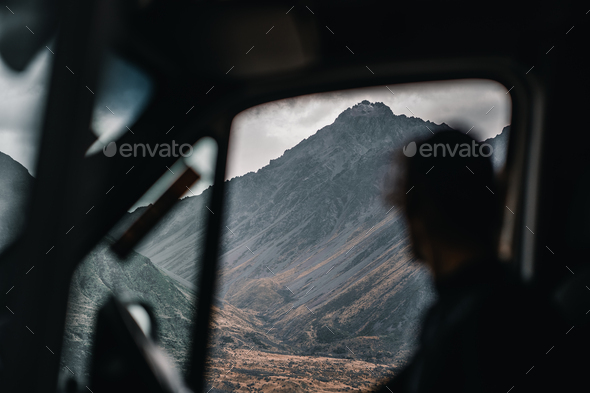defocused silhouette of calm and relaxed caucasian young man inside a car looking at the mountain