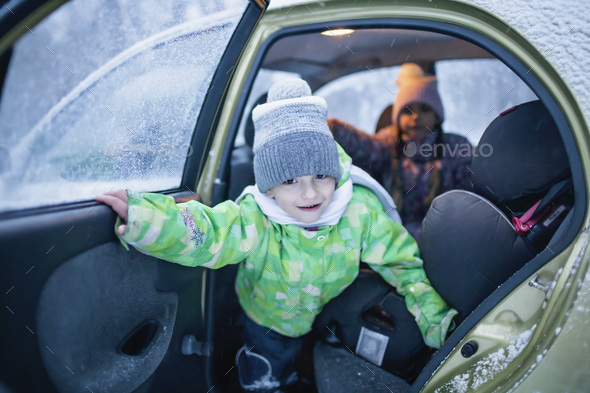 Boy looks out of a car door during a family road trip to the winter forest. Active weekend