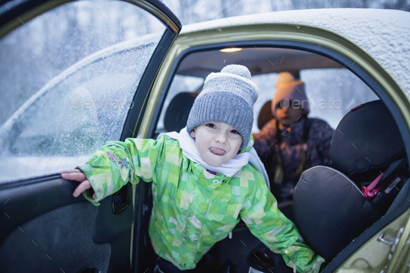 Boy looks out of a car door during a family road trip to the winter forest. Active weekend