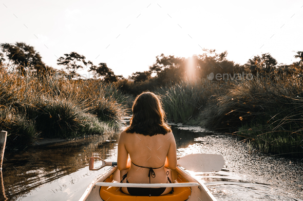 calm relaxed young woman sitting inside a kayak dressed in a swimsuit and holding the paddle against