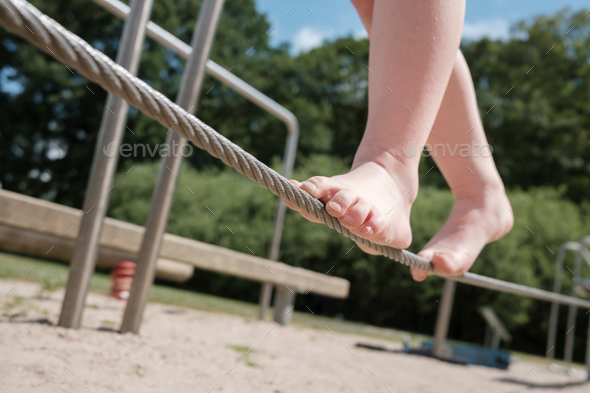 Kid tightrope walker balances with bare feet on a cord