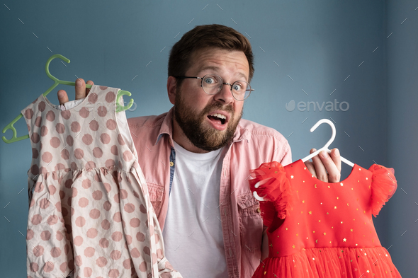Father holds children dresses and looks inquiringly, hoping daughter will finally make choice