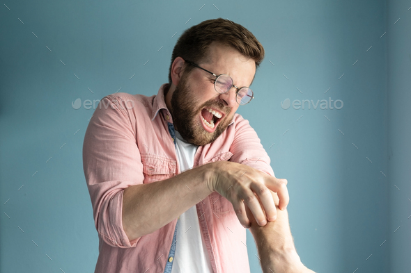 Unhappy annoyed man scratches itchy skin on arm and screams from the unpleasant sensation
