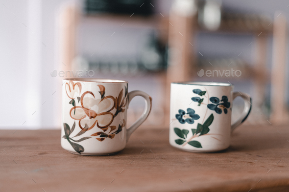 two porcelain cups side by side of the same size decorated with neat flowers on a brown wooden table