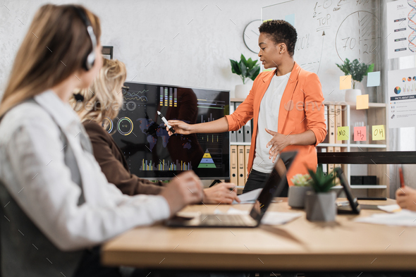 African american woman in orange suit showing financial statistic of enterprise during meeting - Stock Photo - Images