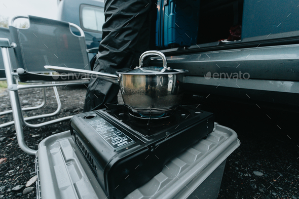 Unrecognizable woman cooking in camping gas during a rainy day.Vanlife lifestyle for urban traveller