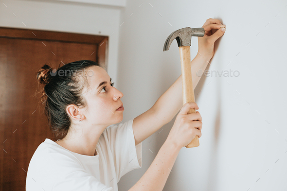 Young woman hammering nail into wall at home to hang a photo frame. home improvement, repair and peo