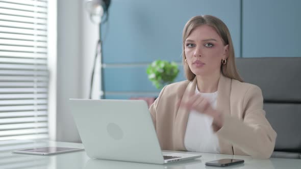 Businesswoman Pointing at the Camera While Using Laptop in Office alt