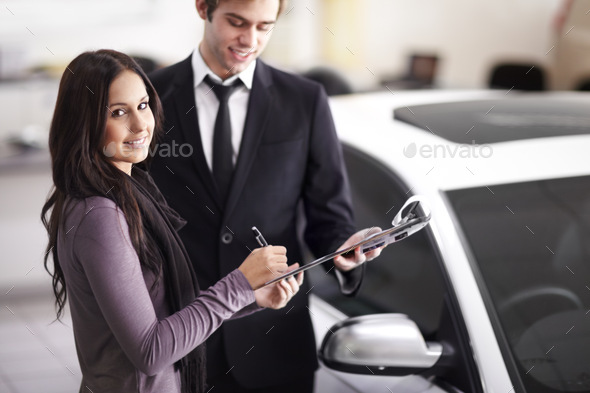 Concluding her vehicle purchase. Attractive young woman signing the paperwork for her new car.