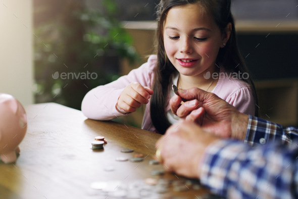 The earlier the better. Shot of a little girl learning about money from her grandfather.