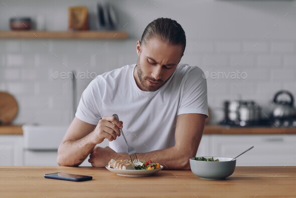 Confident young man eating lunch while sitting at the kitchen counter at home