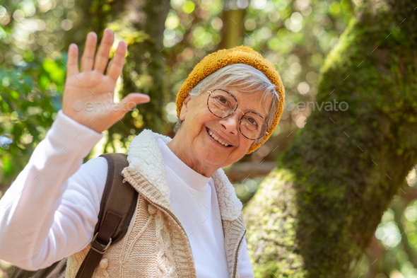 Smiling elderly woman hiking in the woods near a moss covered tree trunk looking at camera
