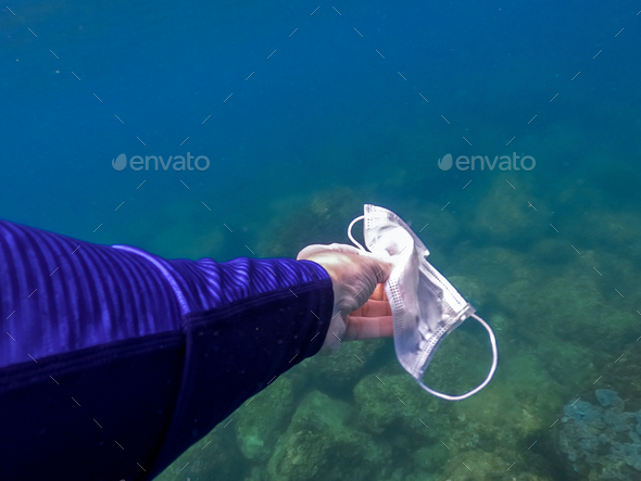 Close up of man hand picking up mask for cleaning area in dirty ocean. Covid-19