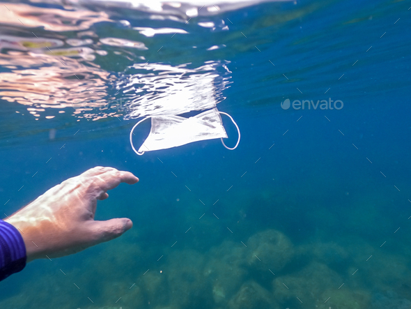 Man hand picking up discarded used disposable medical mask floats in sea waters