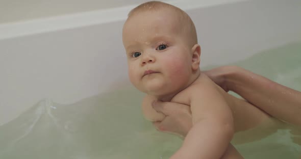 Cute Baby Lying on Mother's Hands Splashing His Palm on the Water in a Bath alt