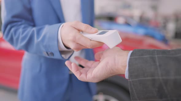 Unrecognizable Car Dealer Measuring Temperature of Client in Dealership with Contactless Thermometer alt