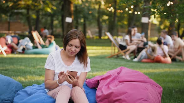 Young Woman Uses a Smartphone in a City Park