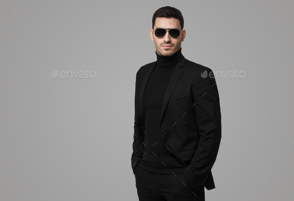 Serious body guard or secret agent wearing suit and sunglasses on grey background