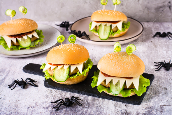 Homemade monster burgers with eyes and tongue for halloween menu on slate and spiders on the table