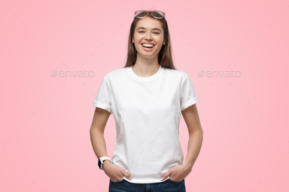 Young girl standing with hands in pockets in blank white t-shirt with copy space, isolated on pink - Stock Photo - Images