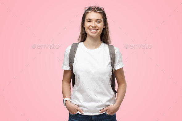 Smiling girl wearing white t-shirt and backpack, isolated on pink - Stock Photo - Images