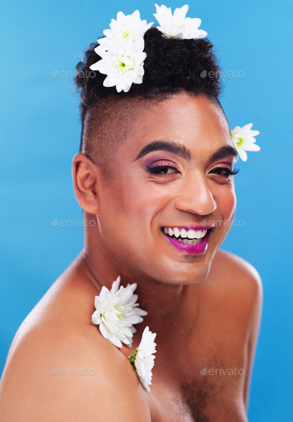 Portrait of a gender fluid young man posing with flowers on his head against a blue background