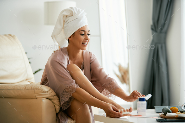 Young woman using nail polish remover while having pedicure at home.
