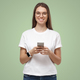 Portrait of attractive young female in white t-shirt, holding smartphone, smiling at camera - PhotoDune Item for Sale