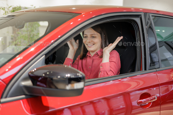 happy woman buys a red car at a car dealership. signing a trade-in contract and handing over keys