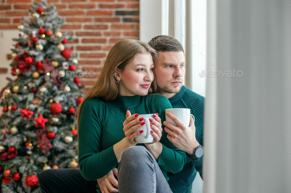 Couple hugs and drinks hot coffee near window. Family, Christmas and winter season concept.