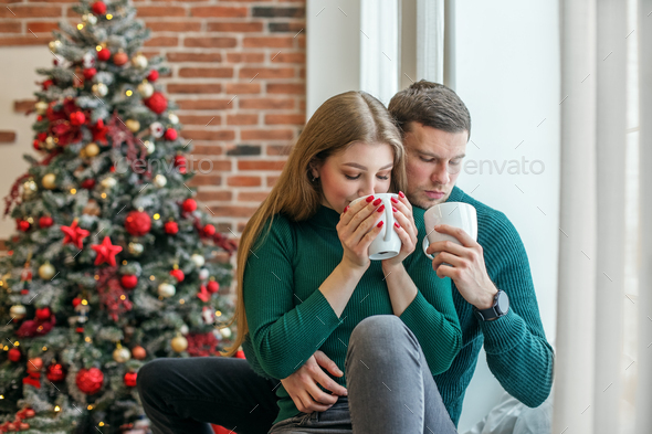 Couple hugs and drinks hot coffee near window. Family, Christmas and winter season concept.