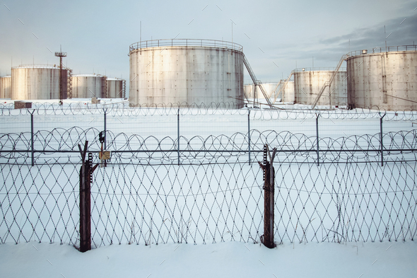 Tank farm of oil storage terminal secured with fence, winter view, snow