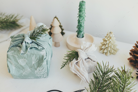 Stylish christmas gift wrapped in fabric on rustic table with