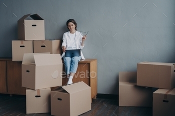 Female with carton boxes searching moving company at laptop for relocation. Transportation service