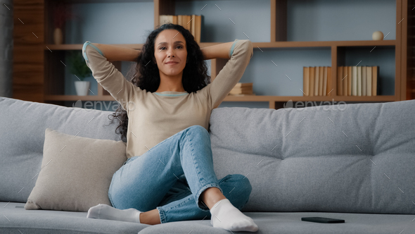 Calm happy in good mood caucasian hispanic latino 30s woman resting on couch new sofa in living room