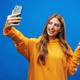 Photo of attractive young woman takes selfie photo on smartphone on blue background - PhotoDune Item for Sale