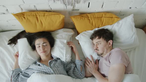 Angry Man and Woman Trying to Sleep in Noisy Apartment Hitting Wall Covering Ears with Pillow alt