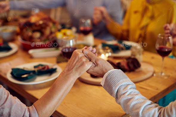 Close-up of senior couple saying grace during Thanksgiving meal with their family.