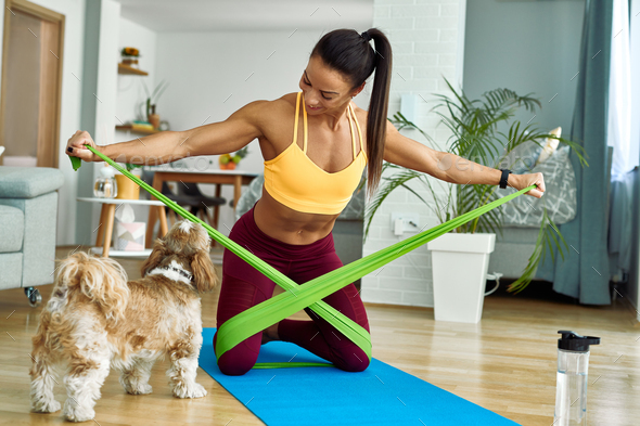 Happy muscular build woman using resistance band while working out in the living room.