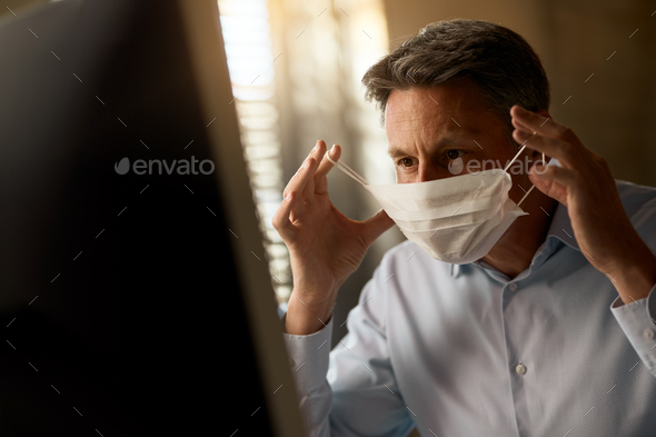 Businessman putting on face mask while working in the office during virus epidemic.