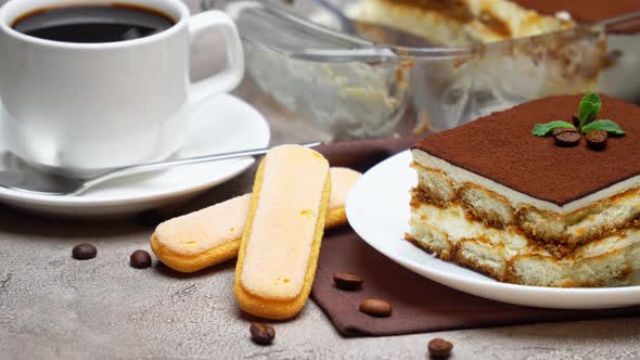 Traditional Italian Tiramisu dessert in glass baking dish and portion on grey concrete background alt