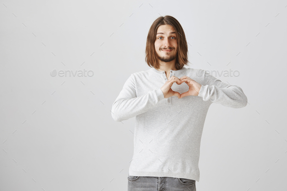 We have same beating of hearts. Portrait of happy romantic caucasian guy with long hair showing