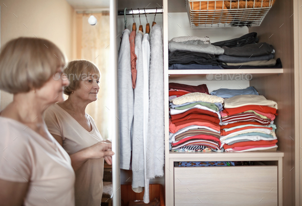 Senior woman choosing outfit from wardrobe. Cleaning, organizing and order in the closet