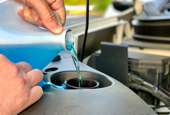 Windshield washer fluid being poured into a vehicle\'s storage tank or reservoir by car’s owner
