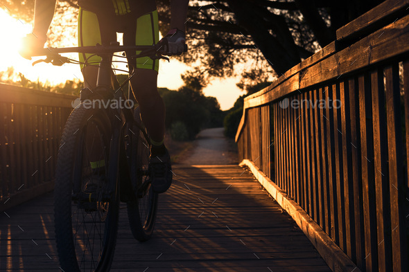 cyclist crossing a wooden bridge at sunset