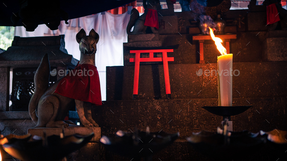 Candle burning in small temple with Kitsune japanese fox statue at Fushimi Inari