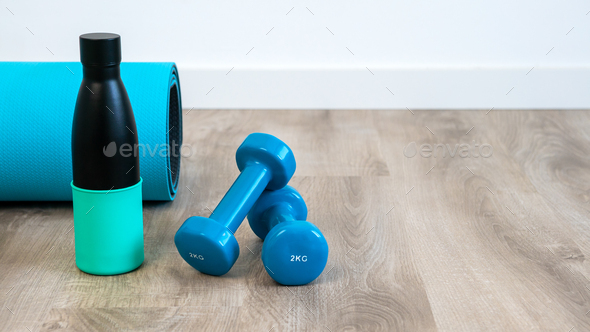 A pair of blue dumbbells and reusable metal water bottle for yoga on floor house