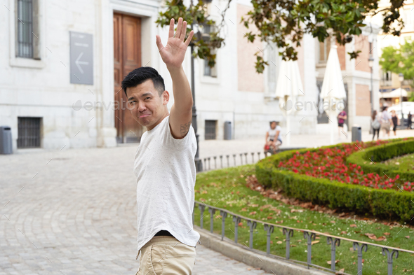 Asian man looking sad while waving hand to say goodbye to someone.