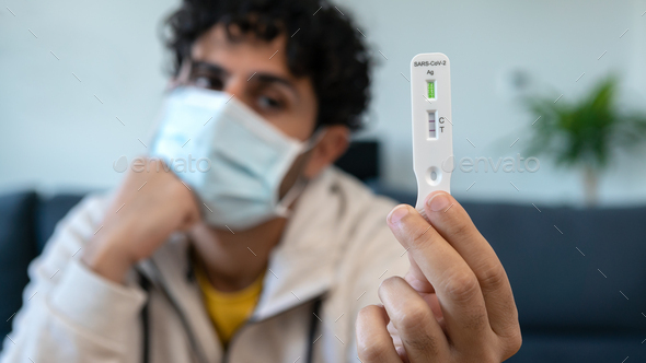 A sad man wearing mask holding a positive sample of covid-19 antigen home test