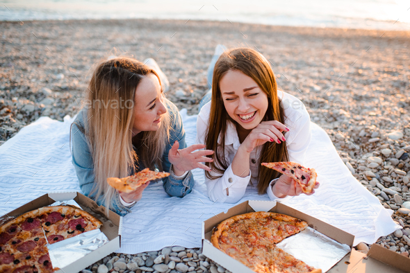 Cheerful young adult girls eating pizza at beach over sea. Vacation season - Stock Photo - Images